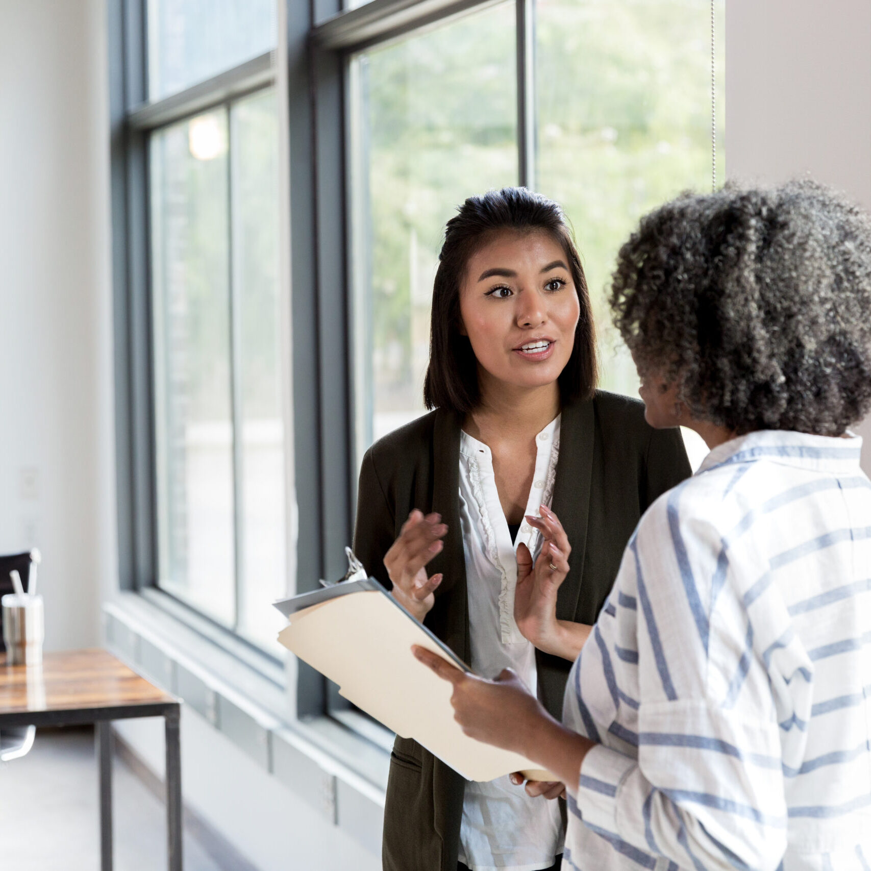 Mature adult female manager and mid adult female employee stand in the conference room and discuss staffing issues.