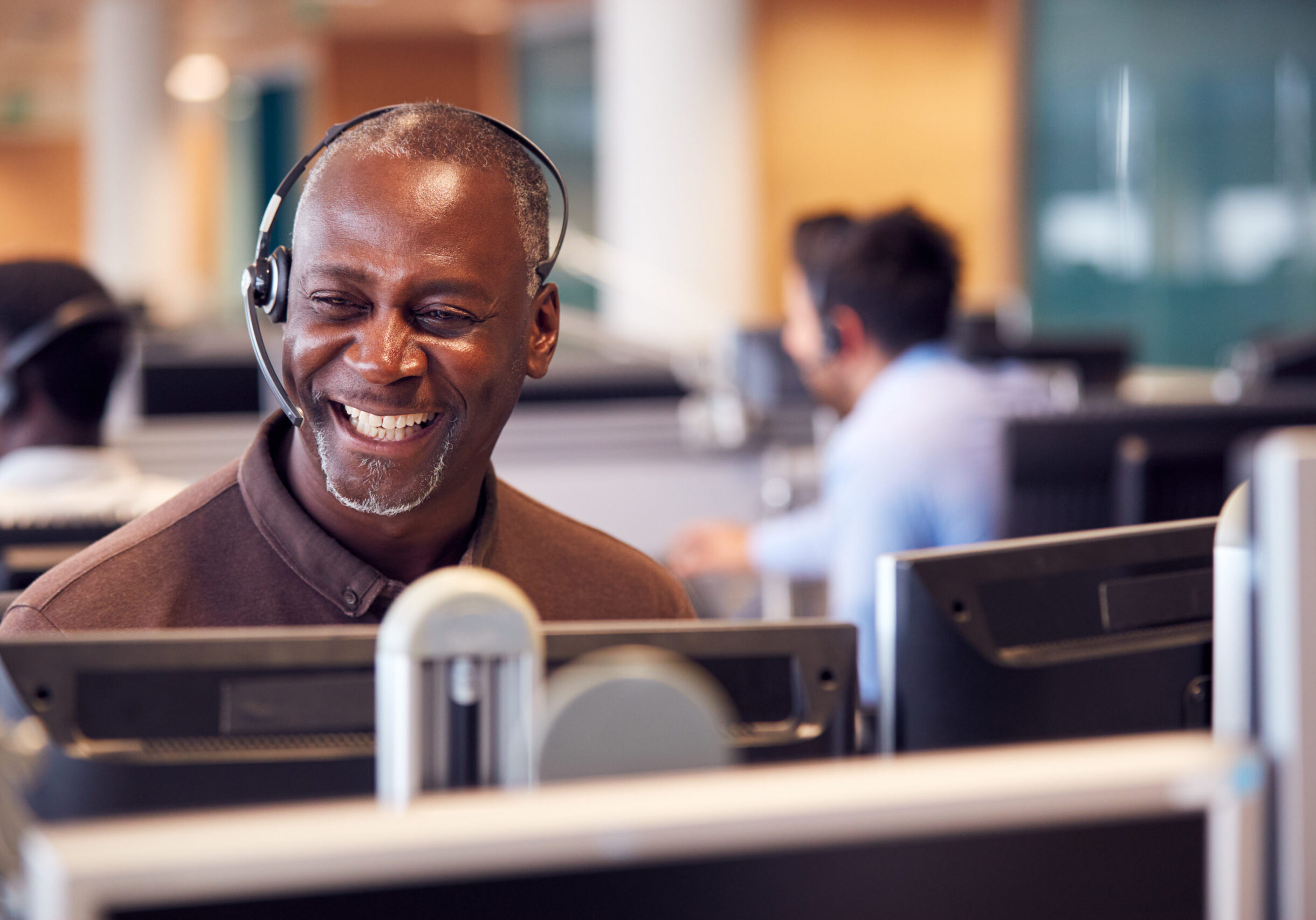 Mature Businessman Wearing Telephone Headset Talking To Caller In Customer Services Department