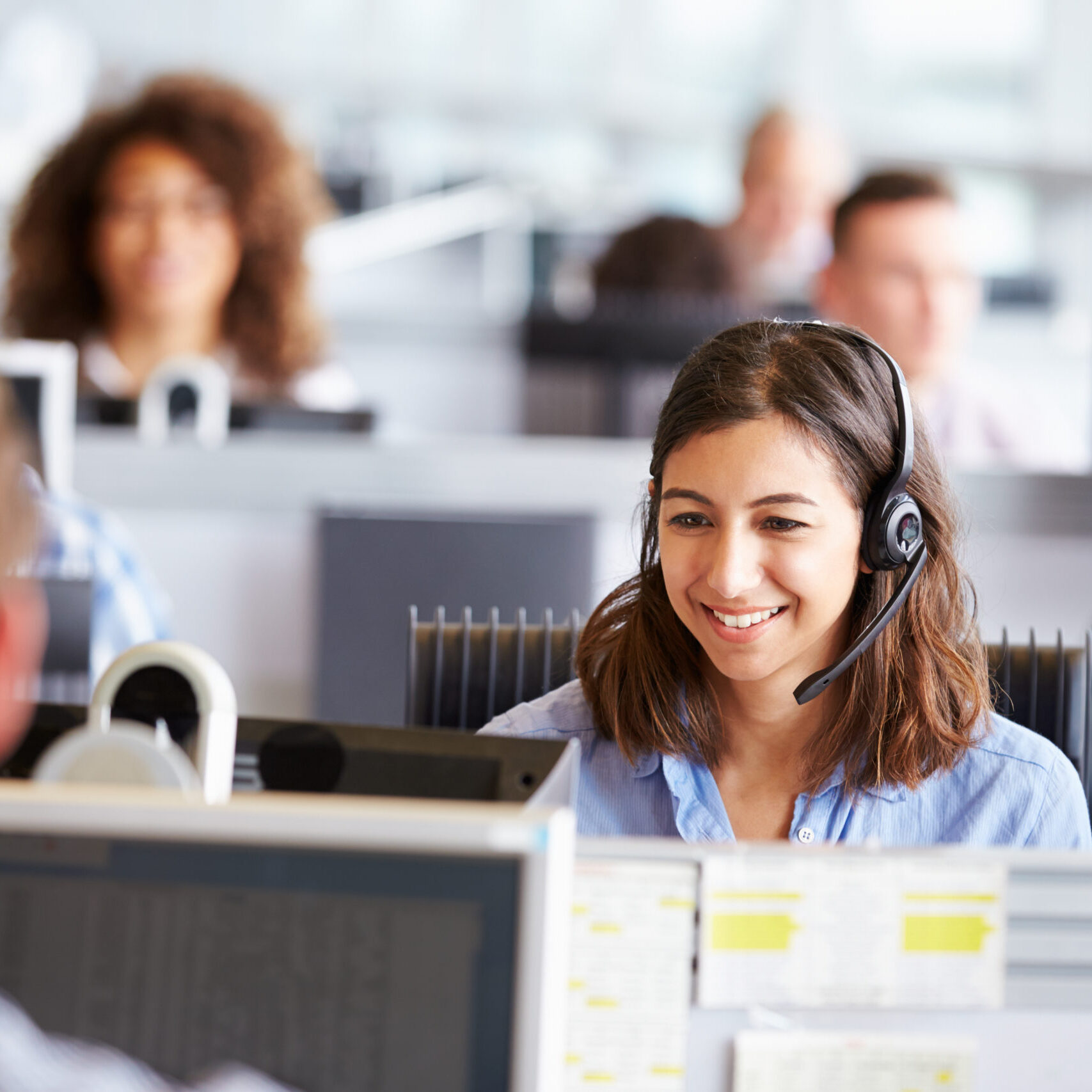 Young woman working in call centre, surrounded by colleagues